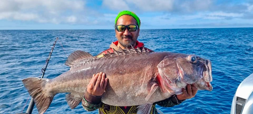 Man on a boat wearing a neon green headband and sunglasses holding a large fish against the open ocean.