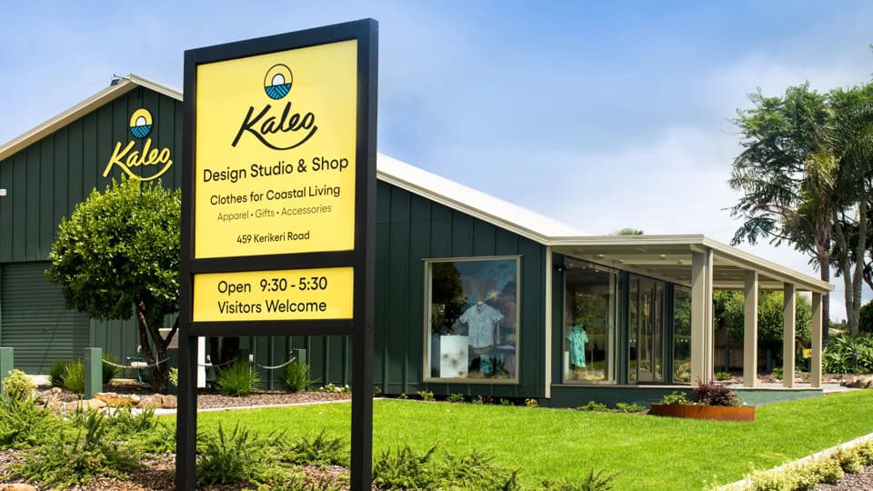 Exterior view of Kaleo Design Studio & Shop building with a tall yellow sign in the foreground, open 9:30–5:30, Visitors Welcome.