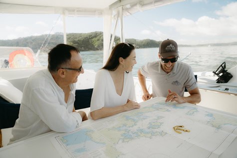 Three people on a boat around a map, planning a route under a bright sky.