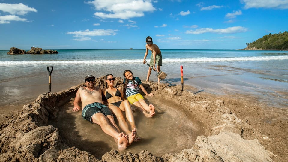 Tourists enjoying a natural hot pool they dug in the sand at Hot Water Beach, New Zealand