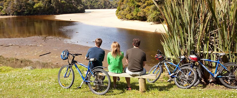 Cyclists pause on a bench with hire bikes, gazing across the estuary on Stewart Island / Rakiura.