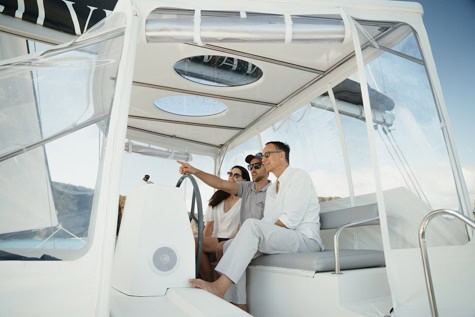 Three adults on a white motorboat; a man in a white shirt points toward the horizon while two passengers look on.