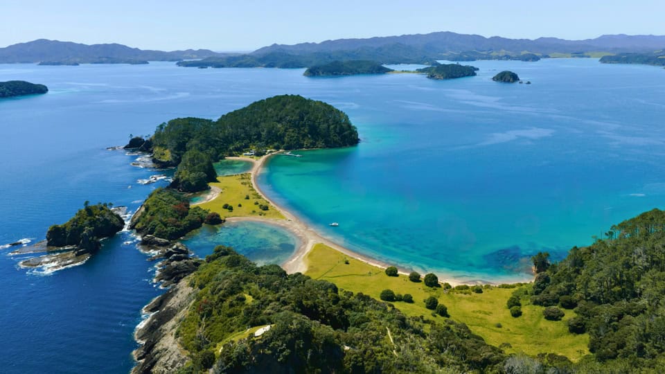 Aerial view of a lush island with a curved sandy beach forming a turquoise bay.