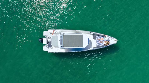 Aerial view of a white motor yacht seen from above, cruising in clear turquoise water with sunlight glinting on the surface.
