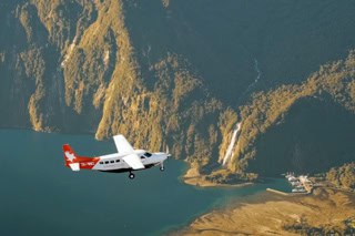 Small red-and-white airplane flying over a rocky coastline and blue water.