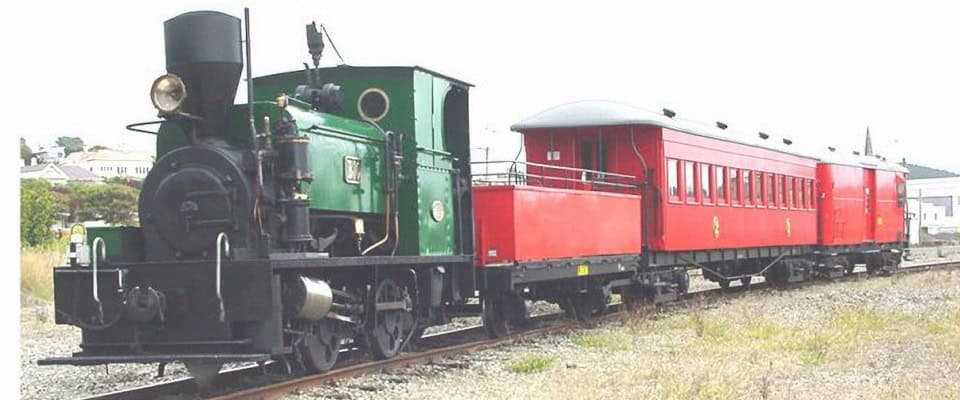 Green steam locomotive pulling bright red passenger cars on a rural railway track. (Vintage train)