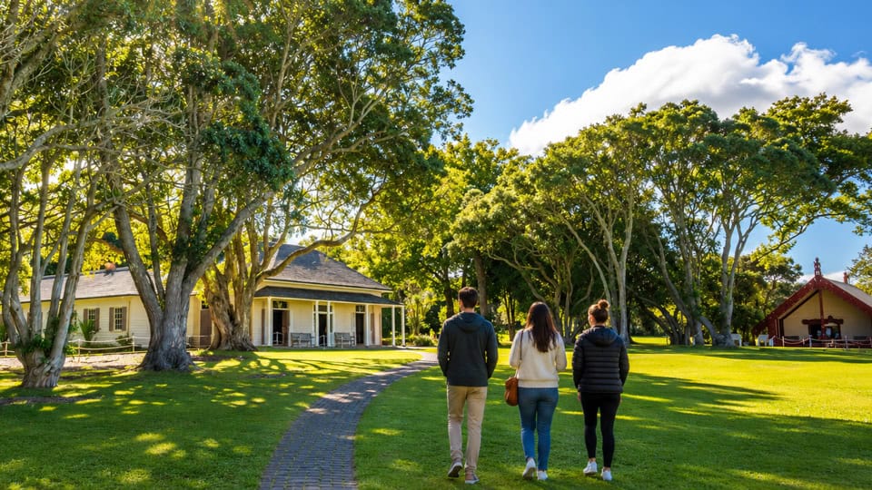 Three people walk along a curved brick path through a sunny park with large trees, a house on the left and a red pavilion on the right?