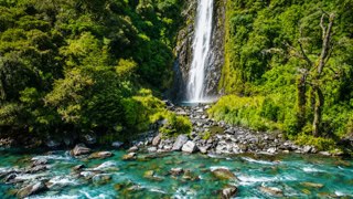 Waterfall cascading into a clear turquoise pool amid a rocky, forested gorge.