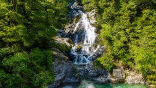 Waterfall cascading over rocks in a lush green forest, flowing into a clear pool below.